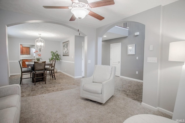 living room with arched walkways, light carpet, baseboards, and ceiling fan with notable chandelier