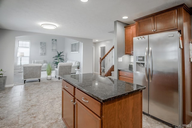 kitchen with stainless steel fridge with ice dispenser, a kitchen island, brown cabinets, open floor plan, and dark stone countertops