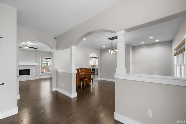 interior space featuring a glass covered fireplace, dark wood finished floors, baseboards, and ceiling fan