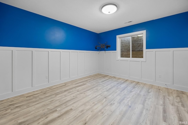 spare room with visible vents, a decorative wall, wood finished floors, and wainscoting