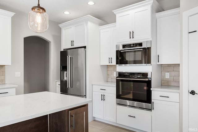 kitchen with tasteful backsplash, arched walkways, white cabinets, appliances with stainless steel finishes, and decorative light fixtures