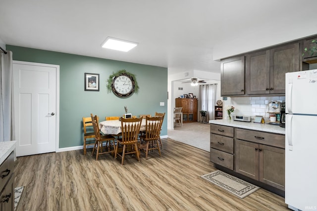 kitchen featuring dark brown cabinetry, tasteful backsplash, light wood-style flooring, freestanding refrigerator, and light countertops