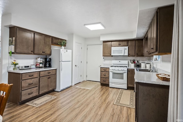 kitchen featuring light countertops, light wood-style flooring, backsplash, a sink, and white appliances