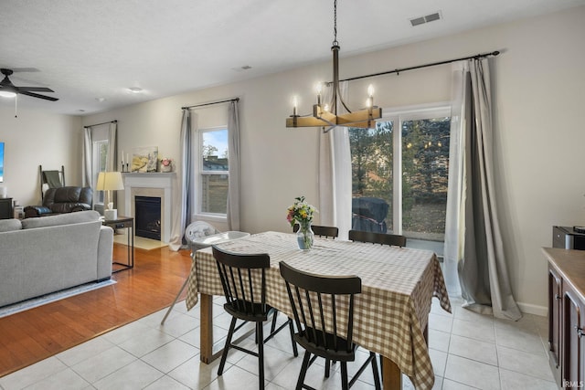 dining area with visible vents, a fireplace with flush hearth, light tile patterned flooring, baseboards, and ceiling fan with notable chandelier