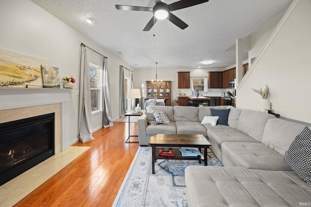 living area with ceiling fan with notable chandelier, a textured ceiling, light wood finished floors, and a premium fireplace