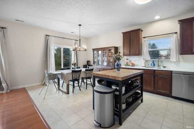 kitchen featuring light tile patterned floors, dishwasher, backsplash, an inviting chandelier, and a sink