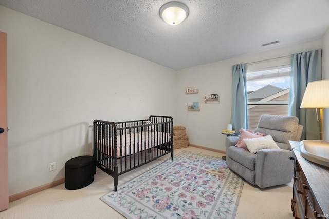 bedroom with baseboards, visible vents, a textured ceiling, carpet floors, and a nursery area