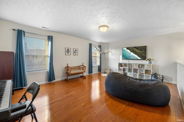 living area with a textured ceiling, hardwood / wood-style flooring, visible vents, and baseboards