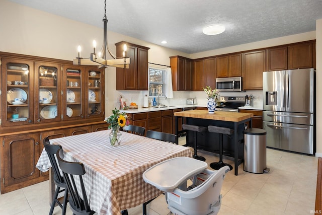 kitchen with light tile patterned flooring, stainless steel appliances, a sink, hanging light fixtures, and decorative backsplash