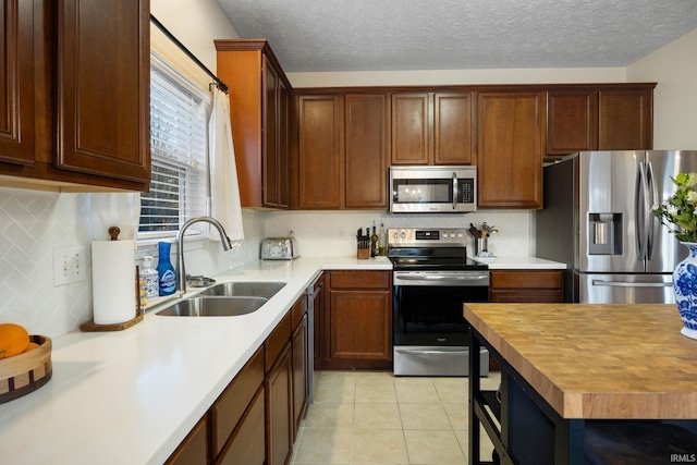 kitchen with light tile patterned floors, backsplash, appliances with stainless steel finishes, a sink, and a textured ceiling