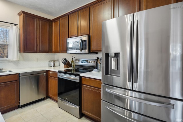 kitchen with decorative backsplash, light countertops, a textured ceiling, stainless steel appliances, and light tile patterned flooring