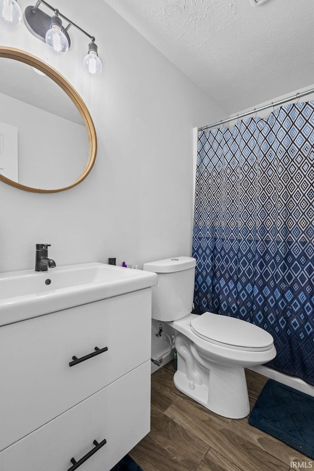 full bathroom featuring toilet, wood finished floors, curtained shower, a textured ceiling, and vanity