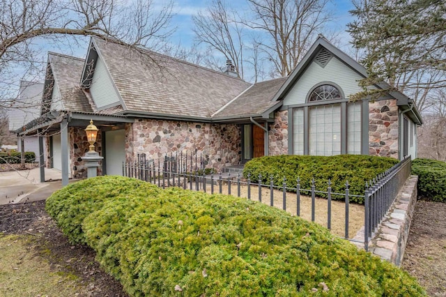 view of front of house featuring a fenced front yard, a garage, stone siding, driveway, and a chimney