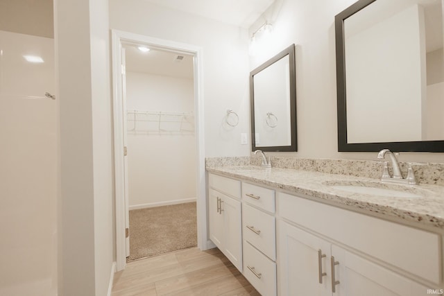 bathroom with wood finished floors, a sink, a spacious closet, and double vanity