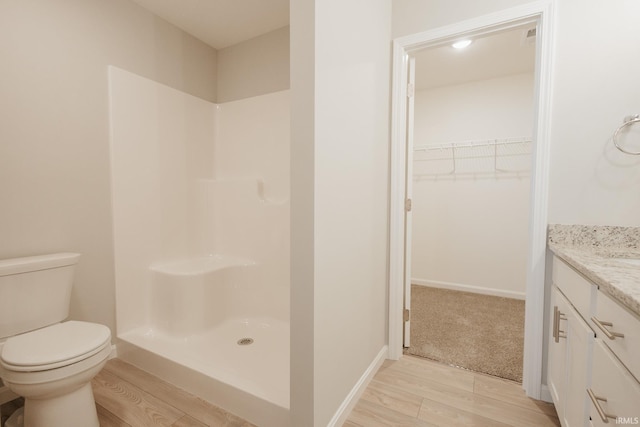 full bathroom with a walk in shower, toilet, wood finished floors, vanity, and a walk in closet