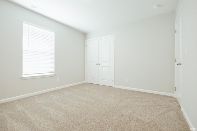 unfurnished bedroom with baseboards, a closet, visible vents, and light colored carpet