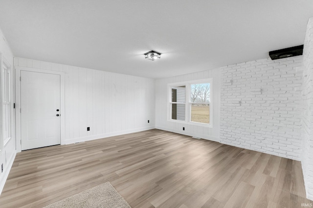 empty room featuring light wood-style floors, baseboards, and brick wall