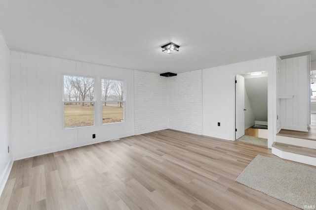 unfurnished room with brick wall, light wood finished floors, and baseboards