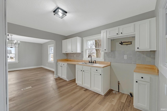 kitchen with light wood finished floors, decorative backsplash, white cabinets, a sink, and baseboards