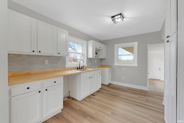 kitchen featuring light wood finished floors, tasteful backsplash, white cabinets, and a sink