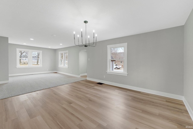 unfurnished dining area with light wood finished floors, visible vents, arched walkways, and a wealth of natural light