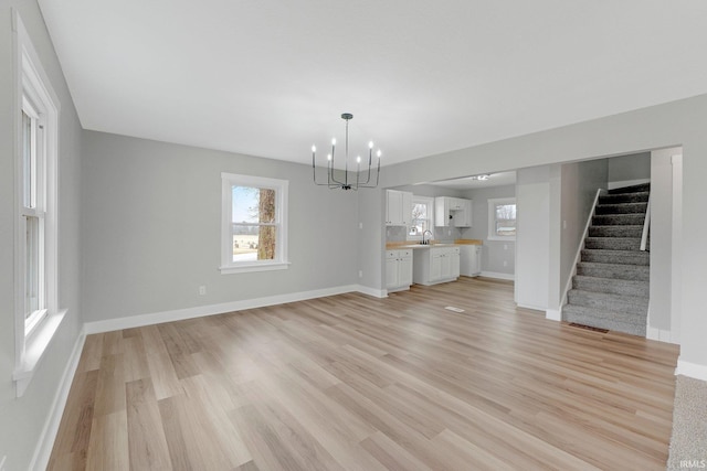 unfurnished living room with a sink, baseboards, stairway, light wood-type flooring, and an inviting chandelier