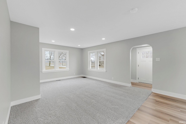 spare room with light wood finished floors, baseboards, visible vents, arched walkways, and recessed lighting