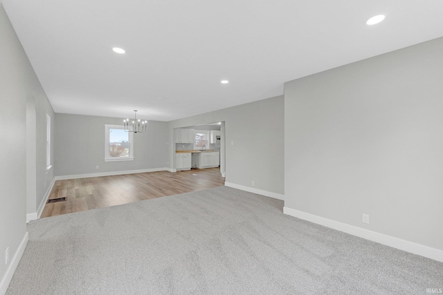 unfurnished living room with carpet floors, baseboards, a notable chandelier, and recessed lighting