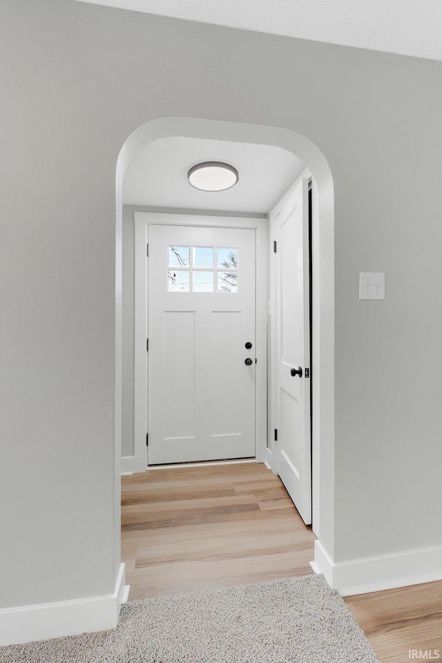 doorway to outside featuring light wood-style floors, baseboards, and arched walkways