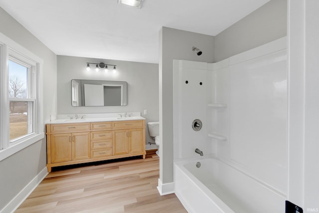 bathroom featuring toilet, double vanity, baseboards, and wood finished floors