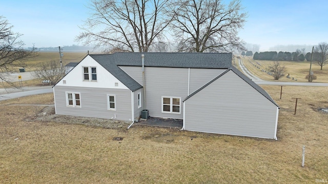 rear view of house featuring a yard, a shingled roof, and central air condition unit