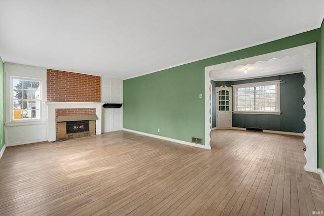 unfurnished living room featuring hardwood / wood-style floors, a fireplace, visible vents, and baseboards