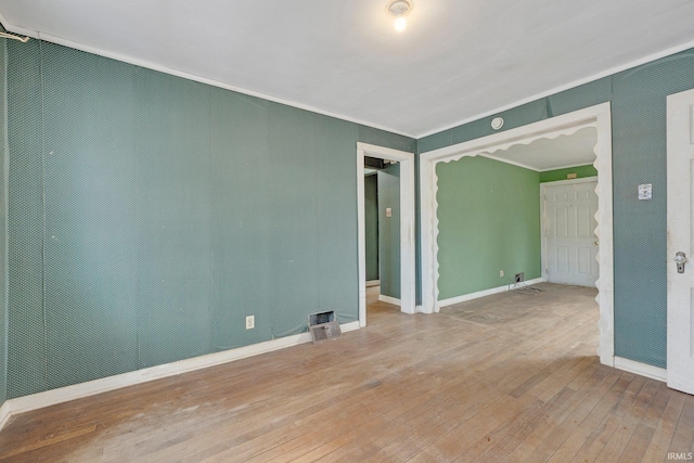 empty room featuring ornamental molding, wood-type flooring, visible vents, and baseboards