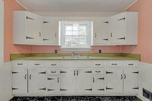 kitchen featuring white cabinets, wainscoting, a sink, and wallpapered walls