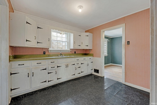 kitchen featuring a sink, visible vents, baseboards, white cabinetry, and crown molding