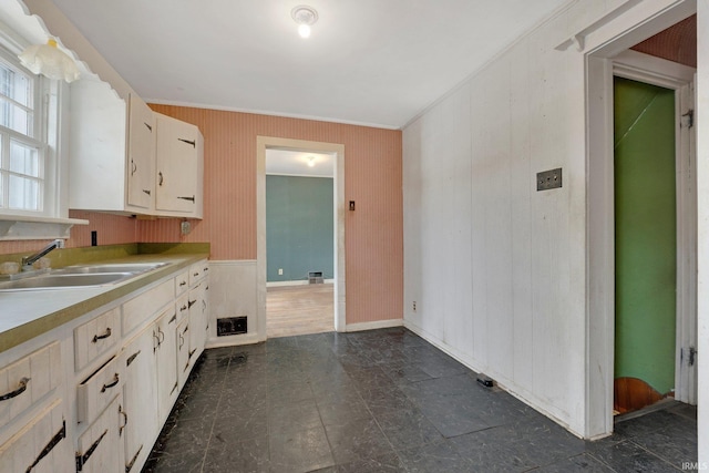 kitchen with baseboards, white cabinets, ornamental molding, light countertops, and a sink