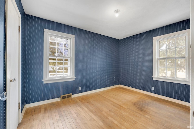 spare room featuring wallpapered walls, baseboards, visible vents, and hardwood / wood-style floors