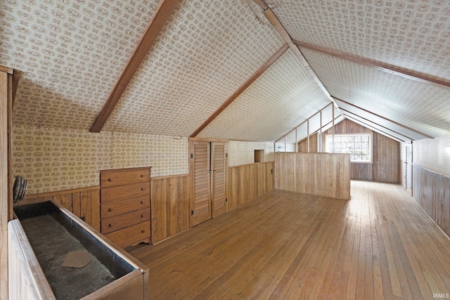 additional living space featuring vaulted ceiling, wood walls, wainscoting, and hardwood / wood-style flooring