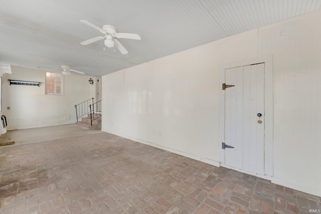 unfurnished room featuring brick floor, stairway, and a ceiling fan