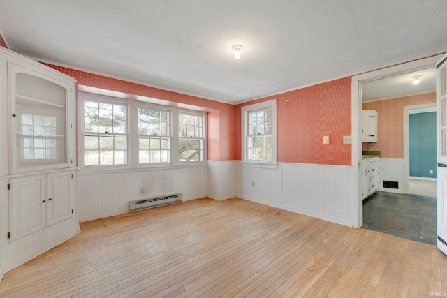 spare room featuring light wood finished floors, a baseboard radiator, visible vents, and a wainscoted wall