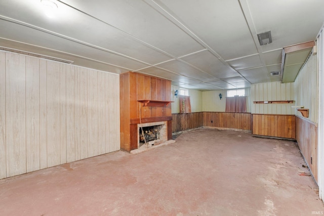 below grade area featuring a fireplace with raised hearth, wood walls, and visible vents