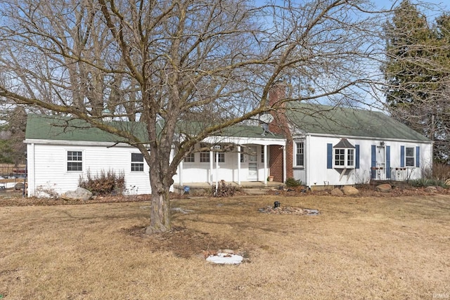 view of front of home featuring covered porch, a chimney, and a front yard