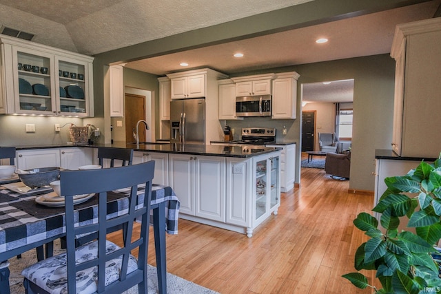 kitchen with stainless steel appliances, dark countertops, visible vents, light wood-style floors, and a peninsula