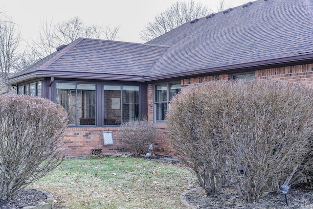 rear view of property with a sunroom, brick siding, a yard, and roof with shingles