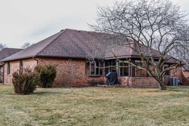 back of house featuring brick siding, a lawn, a shingled roof, and cooling unit