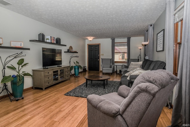 living room featuring light wood finished floors, baseboards, visible vents, and a textured ceiling