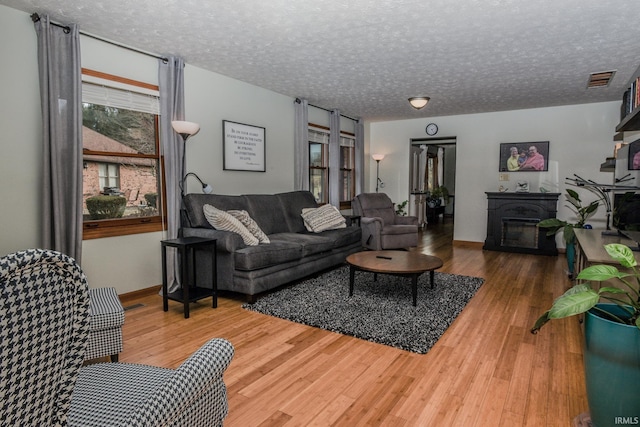 living room featuring a textured ceiling, wood finished floors, visible vents, and baseboards