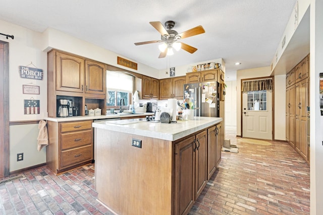 kitchen with brick floor, a sink, baseboards, light countertops, and freestanding refrigerator