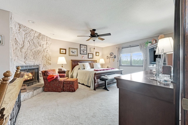 bedroom featuring carpet floors, a ceiling fan, a textured ceiling, and a stone fireplace