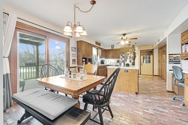 dining area with brick floor, a textured ceiling, and ceiling fan with notable chandelier